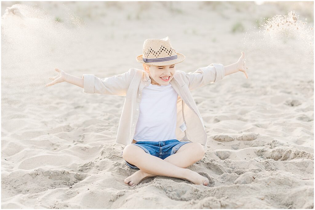 Young boy throws sand in the air during his family's beach photography session in rehoboth beach, delaware